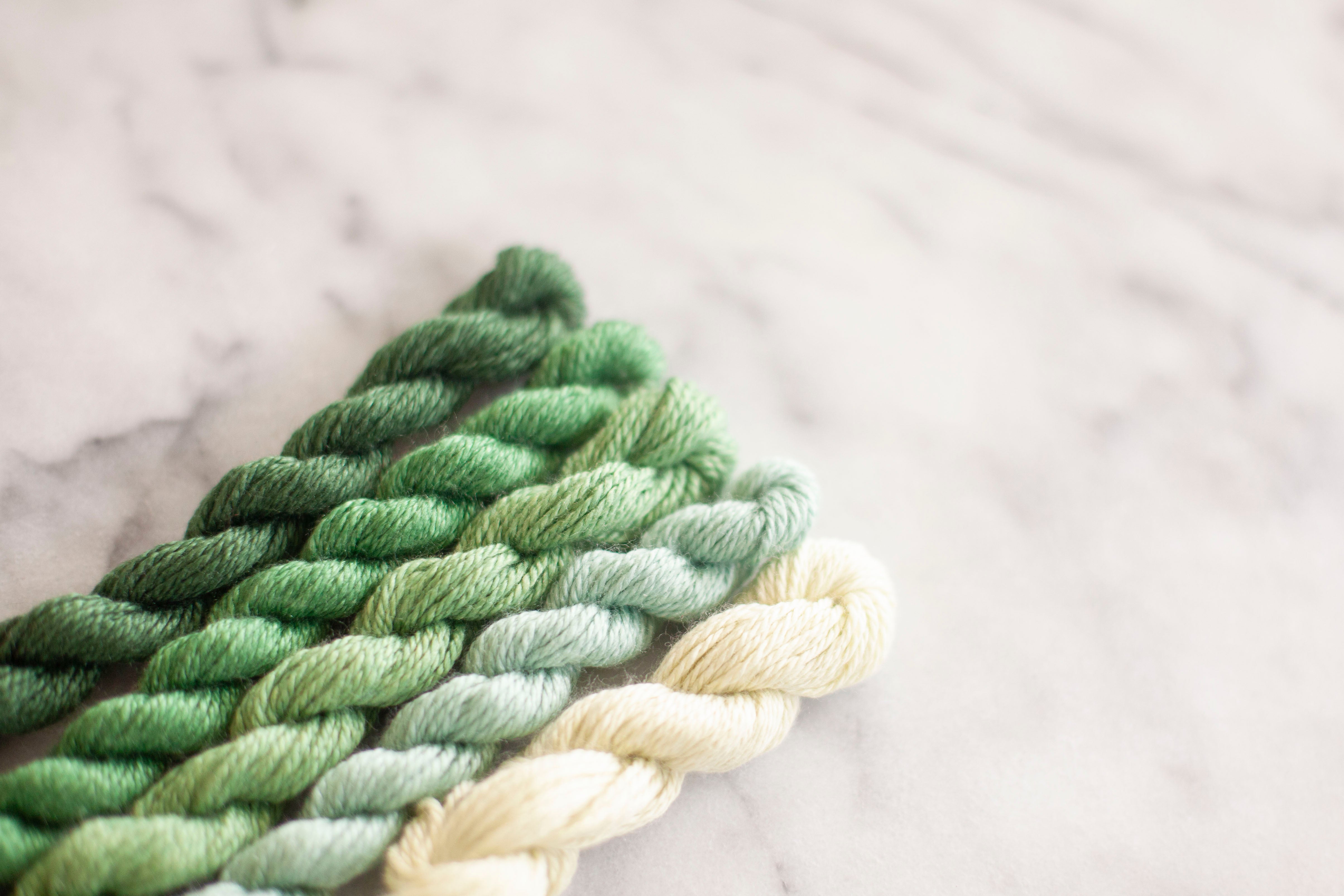 four green skeins of silk and ivory thread arranged from dark to light on a marble surface