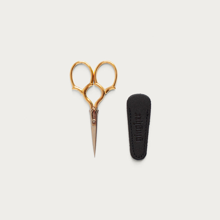 gold handled 3.5" gingher embroidery scissors on off white surface with a black base on the side